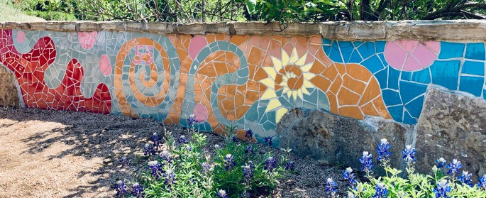 mosaic mural on low stone wall, with bluebonnet flowers